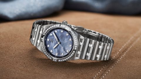 Breitling Chronomat 28 Uhr in Stahl mit Diamantluenette, Rouleauxarmband und Zifferblatt aus blauem Perlmutt seitlich auf braunem Textiluntergrund liegend