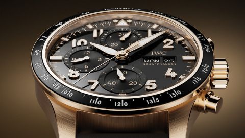 IWC Pilots Watch in Gold mit schwarzer Luenette und Zifferblatt vor braungold-schwarzem Hintergrund IWC Pilots Watch in Gold mit schwarzer Luenette und Zifferblatt vor braungold-schwarzem Hintergrund